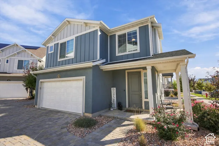 Two-story exterior with a covered entry, attached garage, stone paver driveway, and varied siding