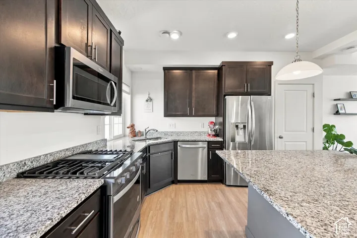 Chef's kitchen featuring dark cabinetry, stainless steel appliances including a gas cooktop and built-in microwave, granite countertops, a large center island, and wood-finish flooring throughout the open layout