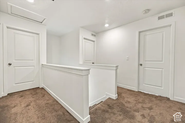 Carpeted landing featuring white doors, recessed lighting, and a white half-wall railing