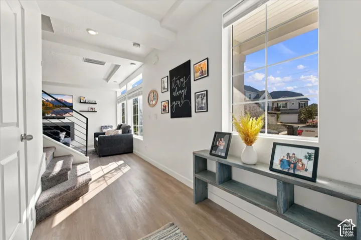 Wood-finish flooring, staircase with metal railing, high ceilings, large window with grid pattern, and recessed lighting