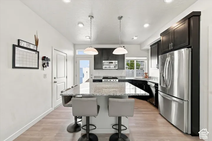 Kitchen featuring a large island with a stone-finish countertop, dark wood-finish cabinetry, stainless steel appliances, and wood-finish flooring