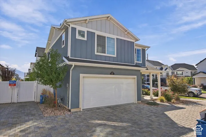Two-story residential exterior featuring a two-car garage, grey stucco, blue vertical siding, and a paver driveway