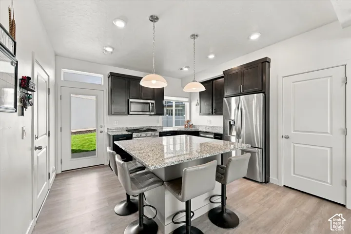 Kitchen with granite-topped island, stainless steel appliances, dark wood cabinetry, and wood-finish flooring