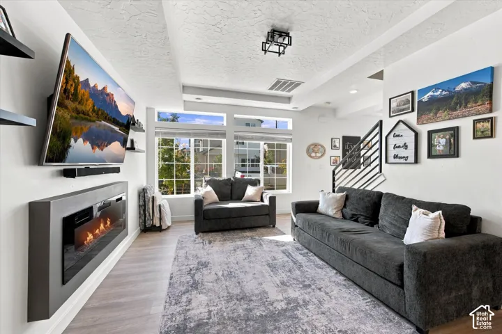 Recessed wall-mounted fireplace with a dark surround, multiple large windows, wood-finish flooring, and a contemporary ceiling light fixture