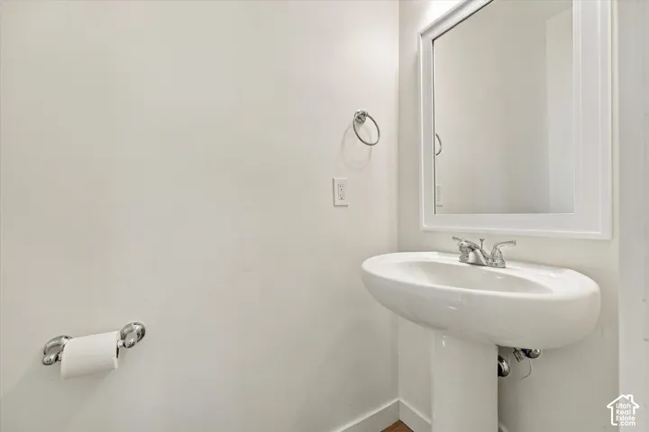 White pedestal sink with a chrome faucet, illuminated by an overhead light, and a framed mirror
