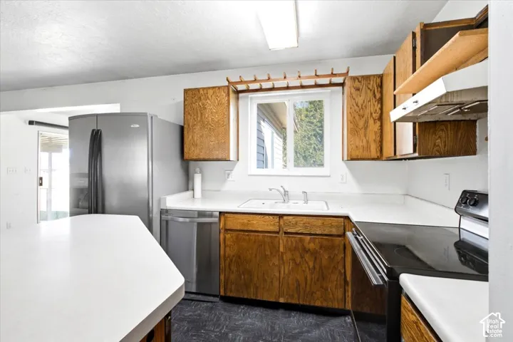 Kitchen featuring wood-finish cabinetry, white countertops, a stainless steel refrigerator, and a stainless steel dishwasher