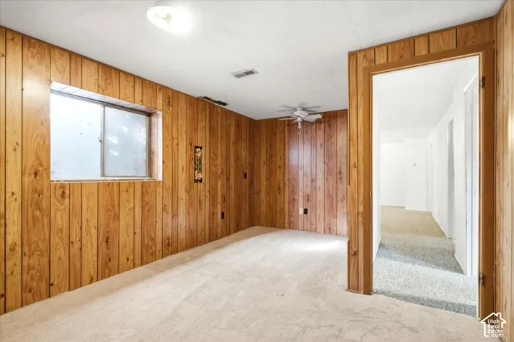 Wood paneling throughout, ceiling-mounted light fixture, window, light-toned carpet flooring, and a ceiling fan