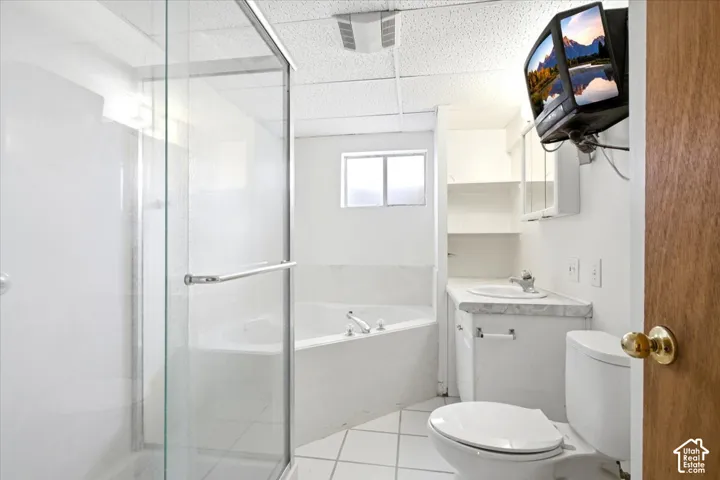 Glass-enclosed shower with chrome hardware, corner soaking tub, white vanity with integrated sink, wall-mounted mirror cabinet, and white tiled flooring