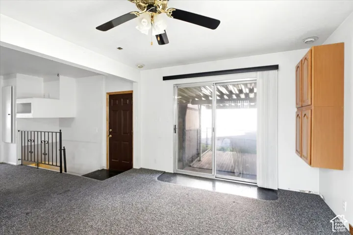 Sliding glass door leading to an exterior deck, brass-finish ceiling fan with lighting, wood-finish wall-mounted cabinetry, wrought iron railing, and a paneled entry door