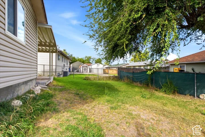 Expansive yard featuring a chain-link fence, mature tree, and a covered patio area