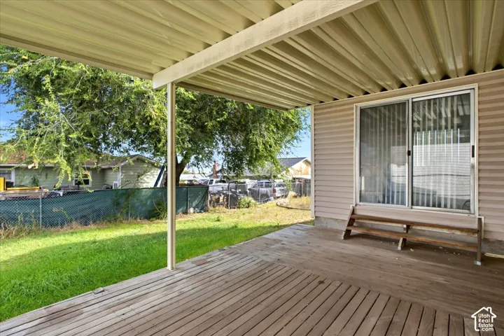 Covered wood-finish patio featuring a sliding glass door entry and a grass lawn