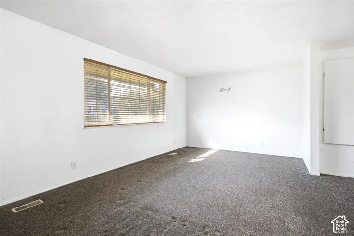 Window with horizontal blinds and wood-finish trim, neutral wall paint, and textured carpeting