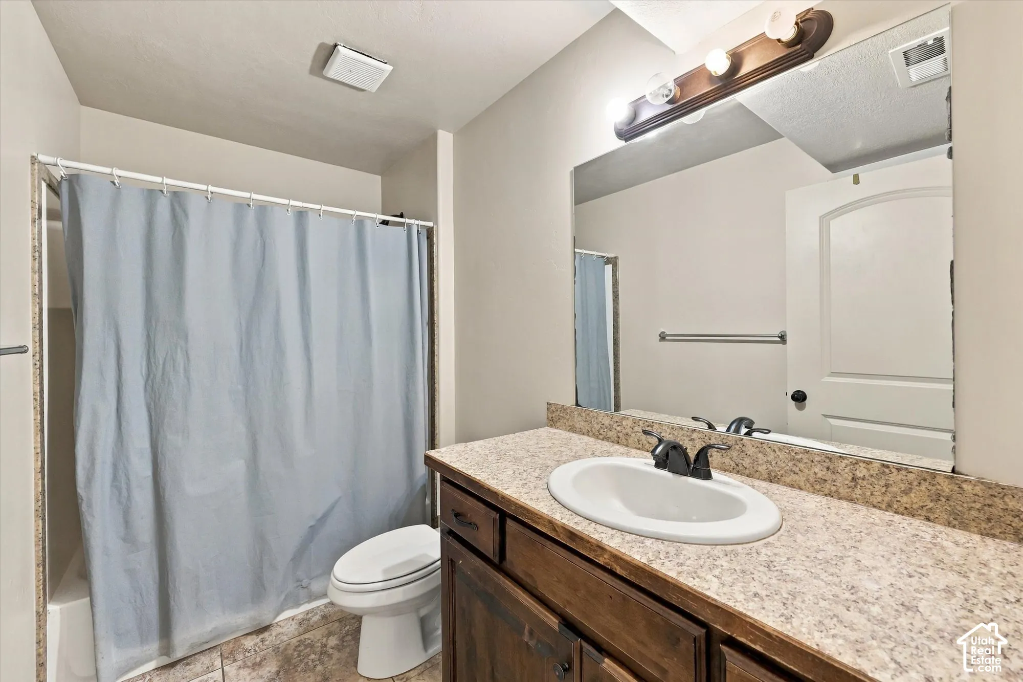 Vanity with integrated sink and dark wood-finish cabinetry, speckled countertop, and wall-mounted mirror