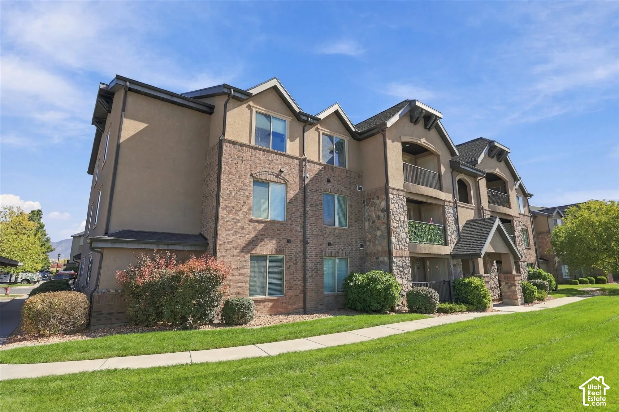 Stucco exterior with brick and stone accents, multiple balconies, gabled rooflines, and a well-maintained lawn