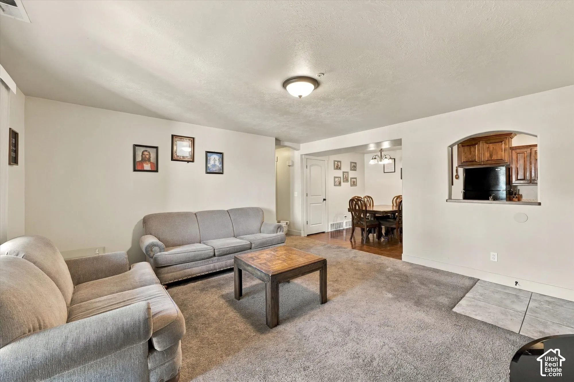 Carpeted living area with neutral walls, an arched pass-through window, and a connected dining area with wood-finish flooring