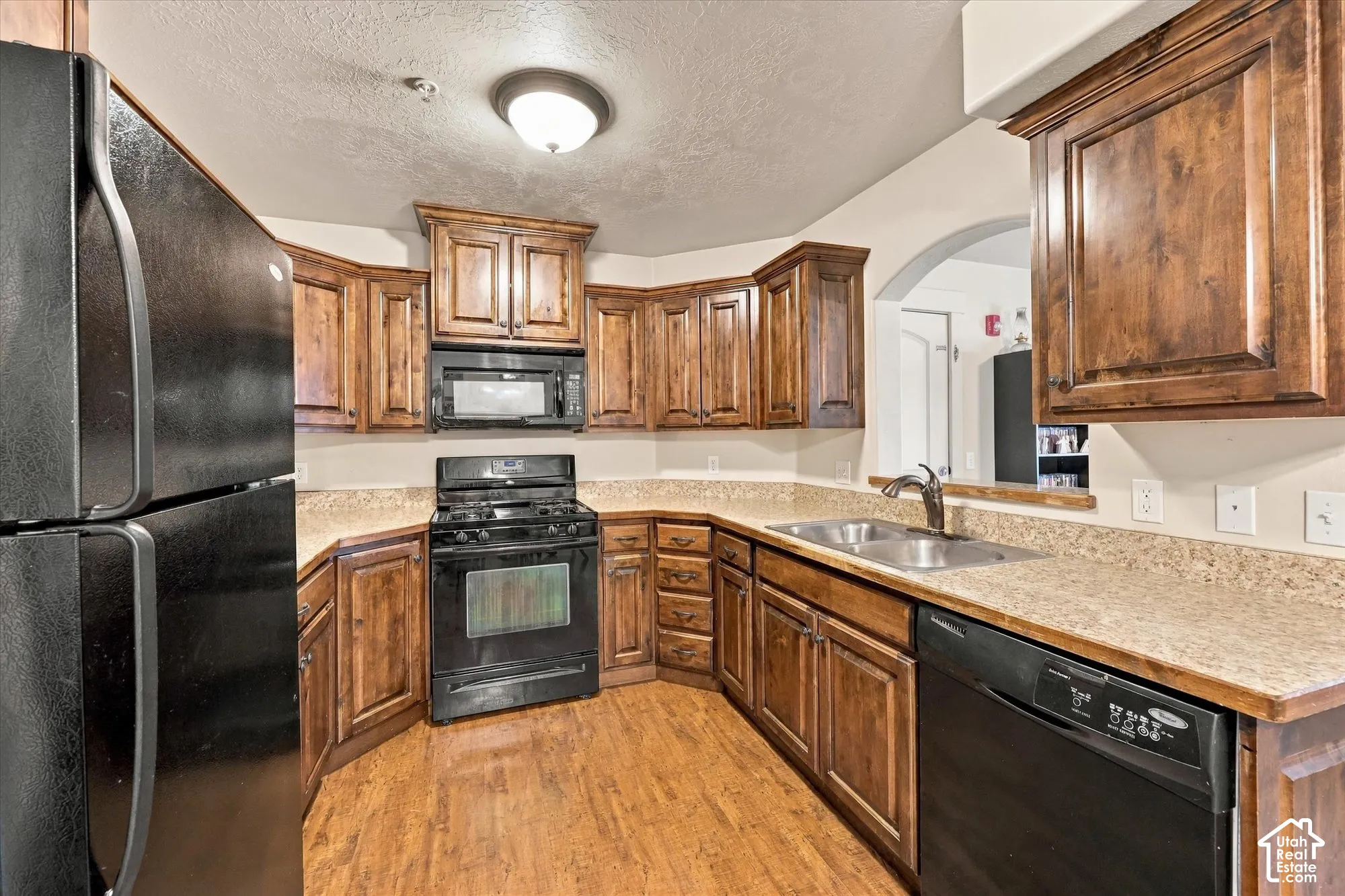 Kitchen featuring wood-finish flooring, dark wood cabinetry, black appliances, and light-toned countertops