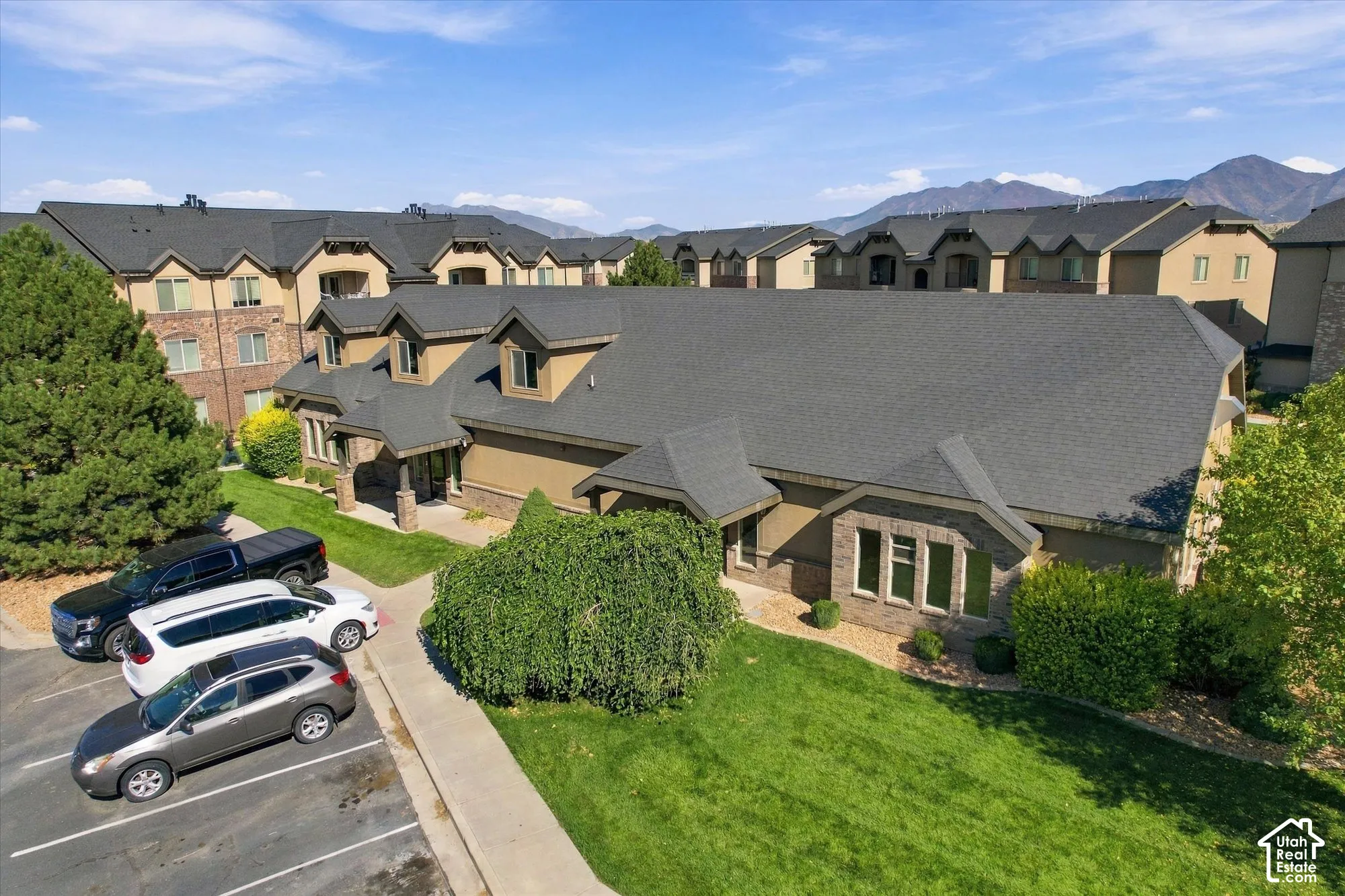 Multi-level property featuring a dark shingle roof, stone and stucco exterior, dormer windows, and a concrete walkway