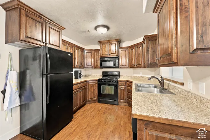 Kitchen featuring wood-finish cabinetry, granite-style countertops, black appliances, a stainless steel double basin sink, and wood-finish flooring