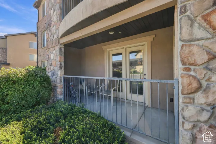 Private covered patio with concrete flooring, framed by mature shrubs and a stone-clad exterior