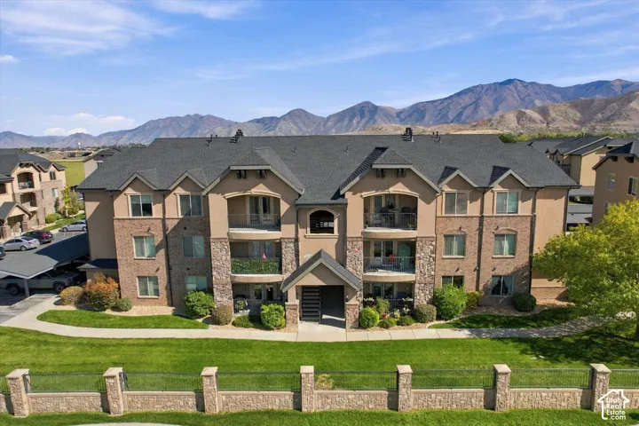 Stately multi-story building featuring a pitched roof, stone and stucco facade, private balconies, and covered parking