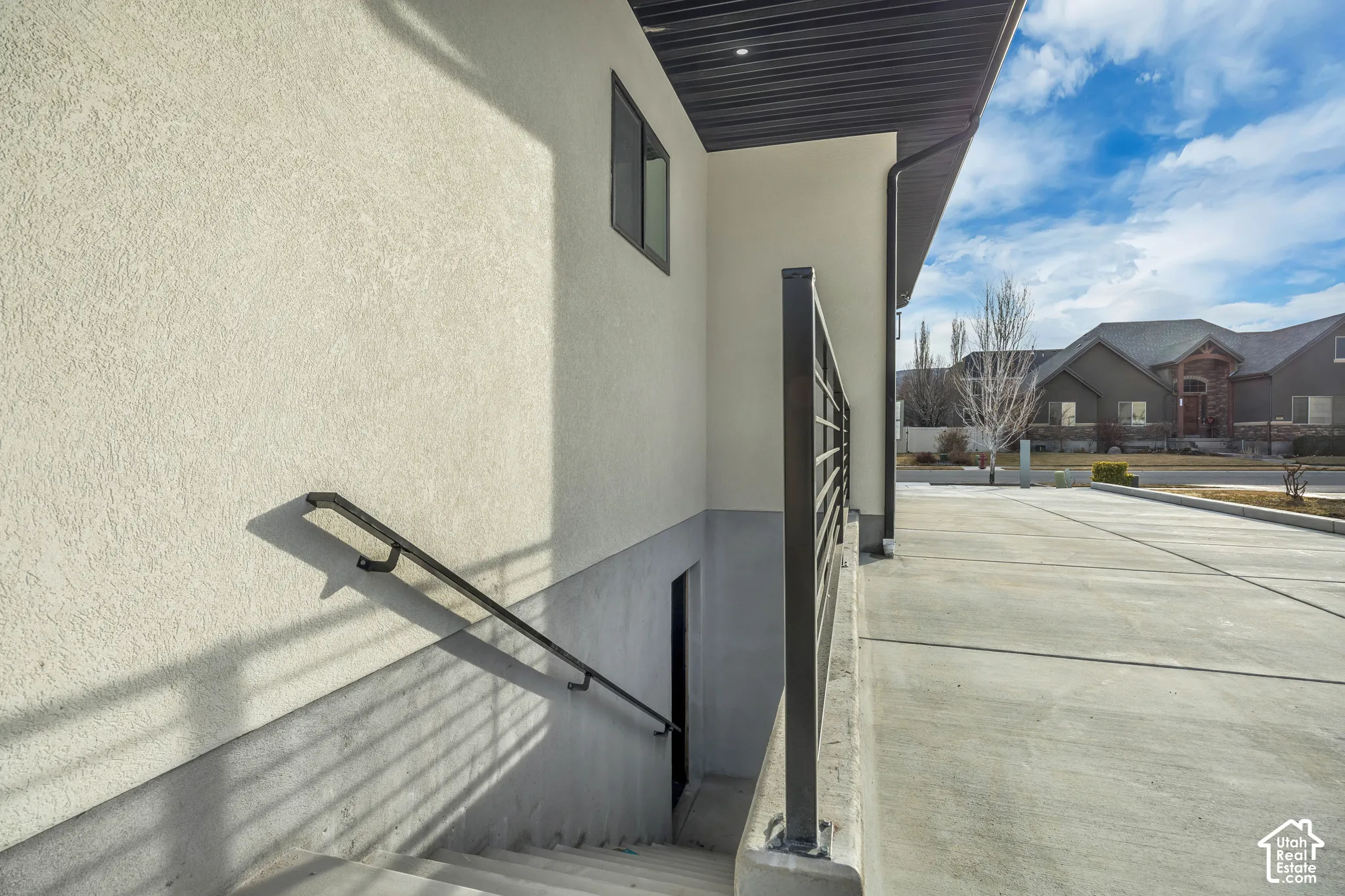 Stucco exterior with a compact window, concrete steps with a black metal handrail, and a concrete driveway