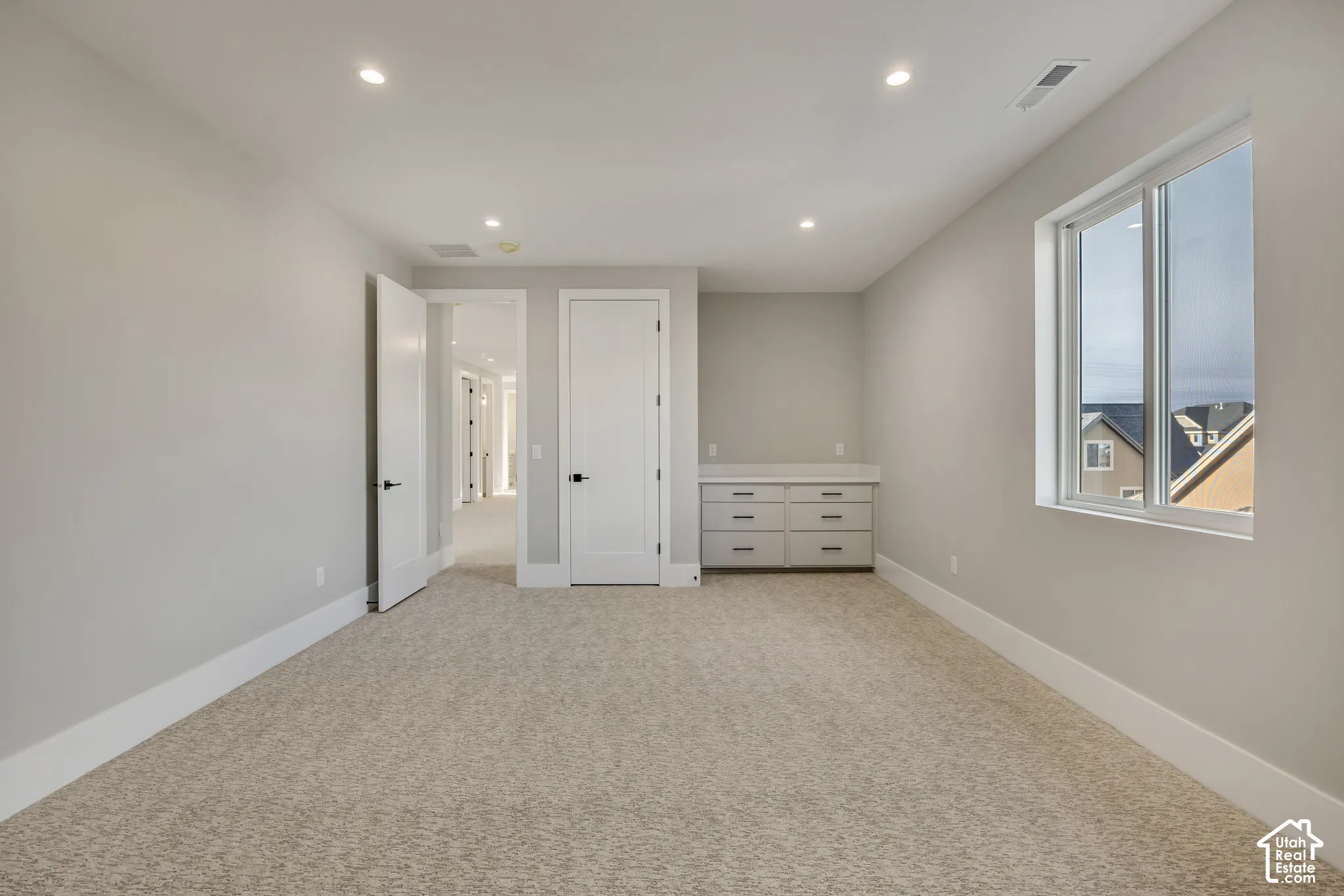Recessed lighting illuminates this room featuring carpet flooring and a built-in cabinet with six drawers and a light-toned countertop