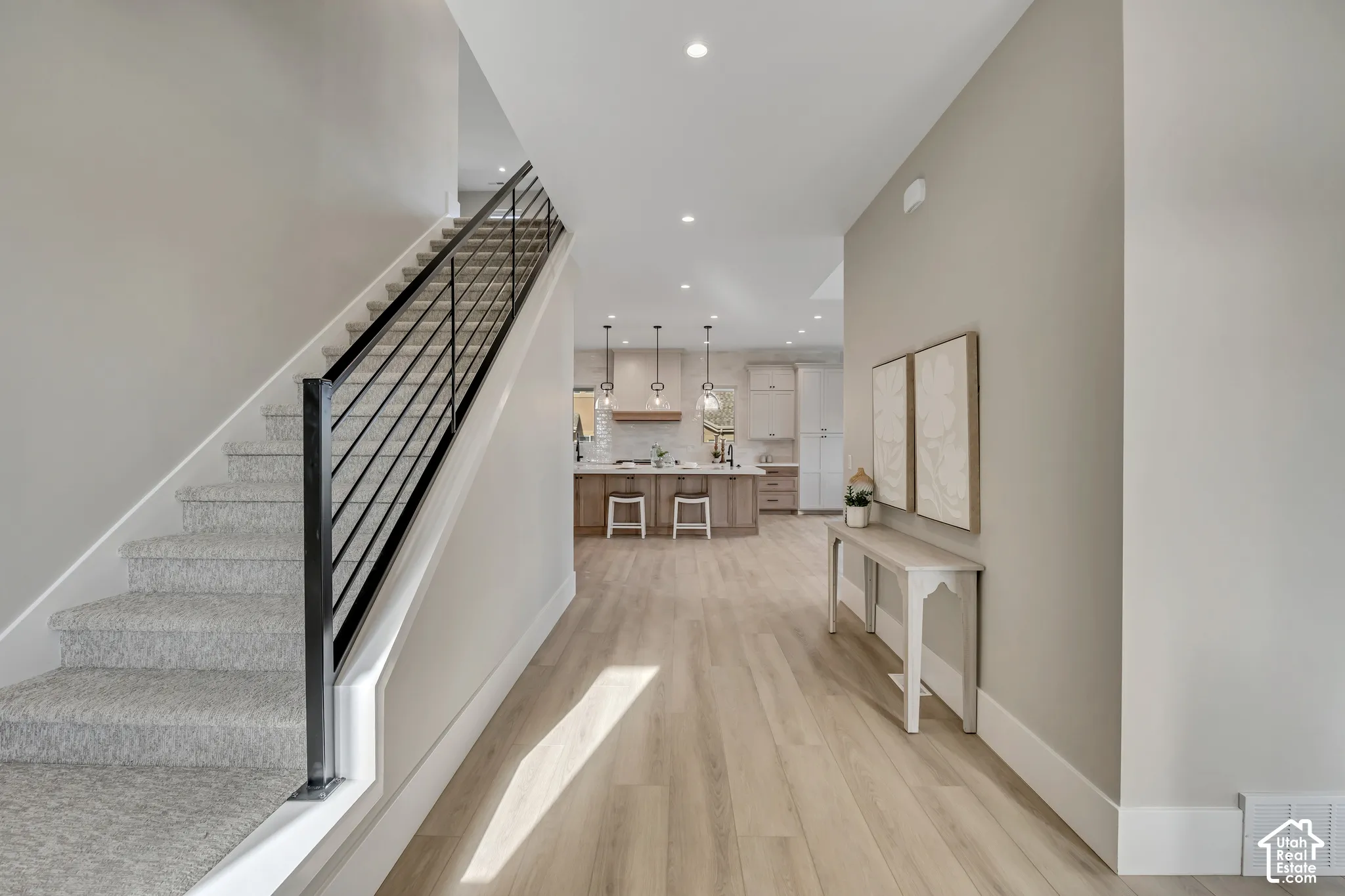 Modern hallway featuring wide-plank wood-finish flooring, recessed ceiling lighting, and a contemporary staircase with black metal railing and gray carpeted treads
