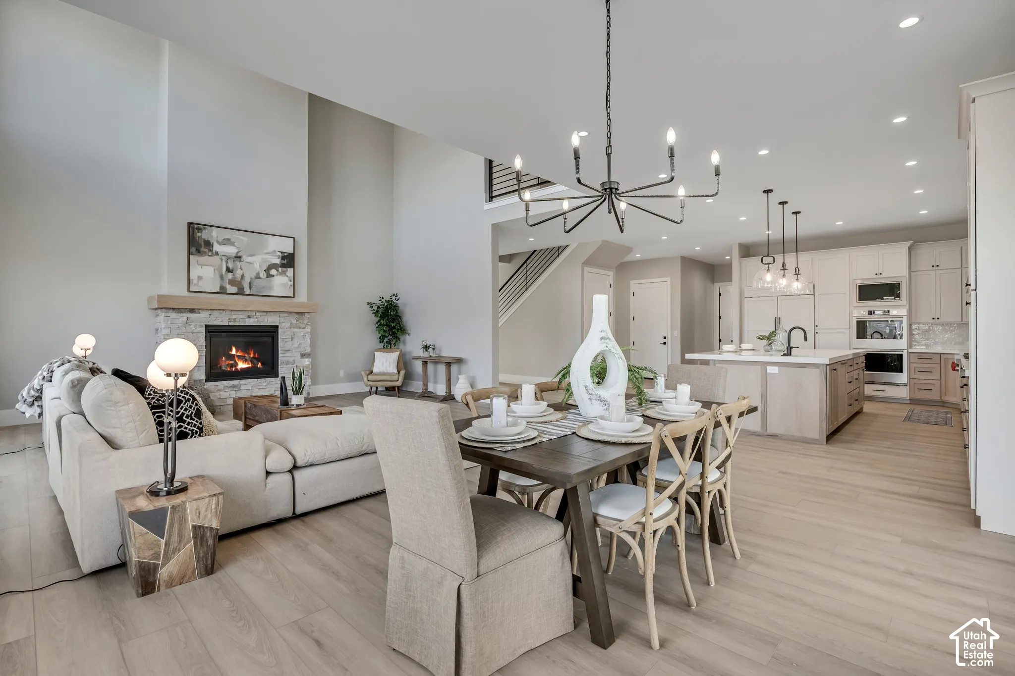 Vaulted ceiling, stone surround fireplace with wood mantel, wood-finish flooring, built-in kitchen appliances, and kitchen island with pendant lighting