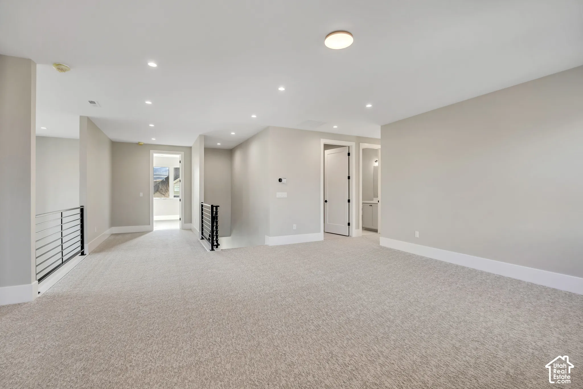 Spacious room with light-toned carpet, recessed lighting, and modern black railings