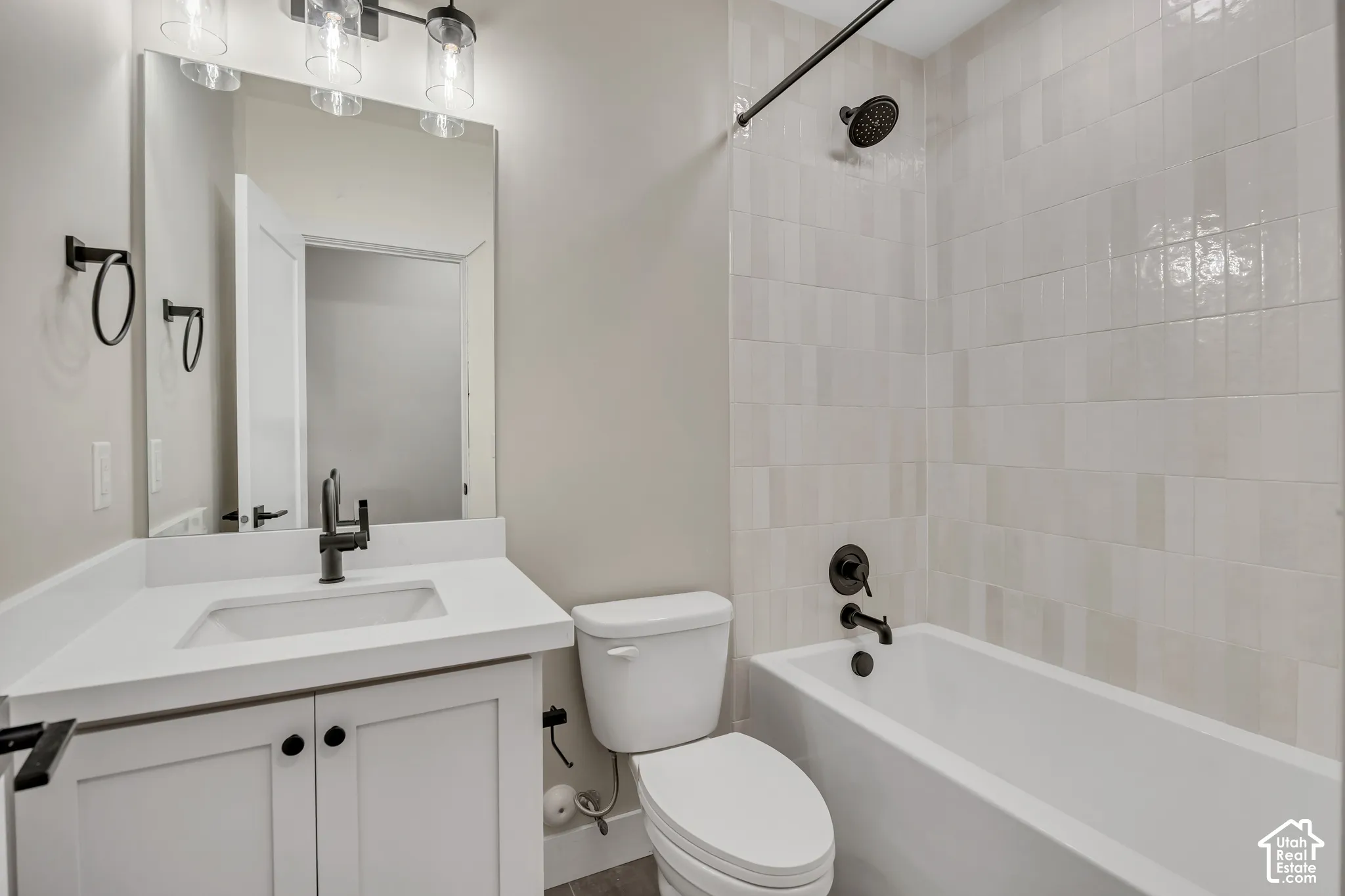 Bathroom featuring a white vanity with integrated sink, matte black fixtures, an overhead light bar, and a tiled shower-tub combination