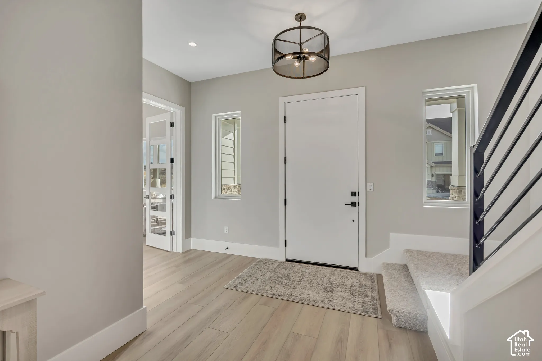 Light wood-finish flooring, white entry door, contemporary black metal chandelier, carpeted staircase, and French pane doors