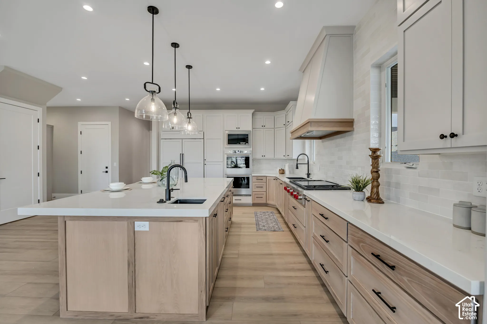 Spacious kitchen featuring an expansive center island with an integrated sink, light wood-finish cabinetry, white countertops, and a full suite of stainless steel appliances