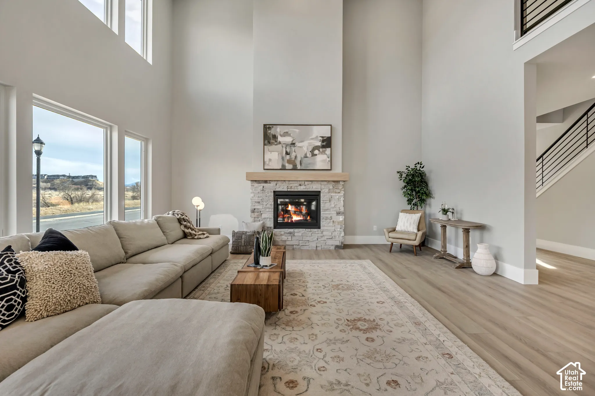 Two-story living area featuring a stone-faced fireplace with a wood mantel, wood-finish flooring, and large windows
