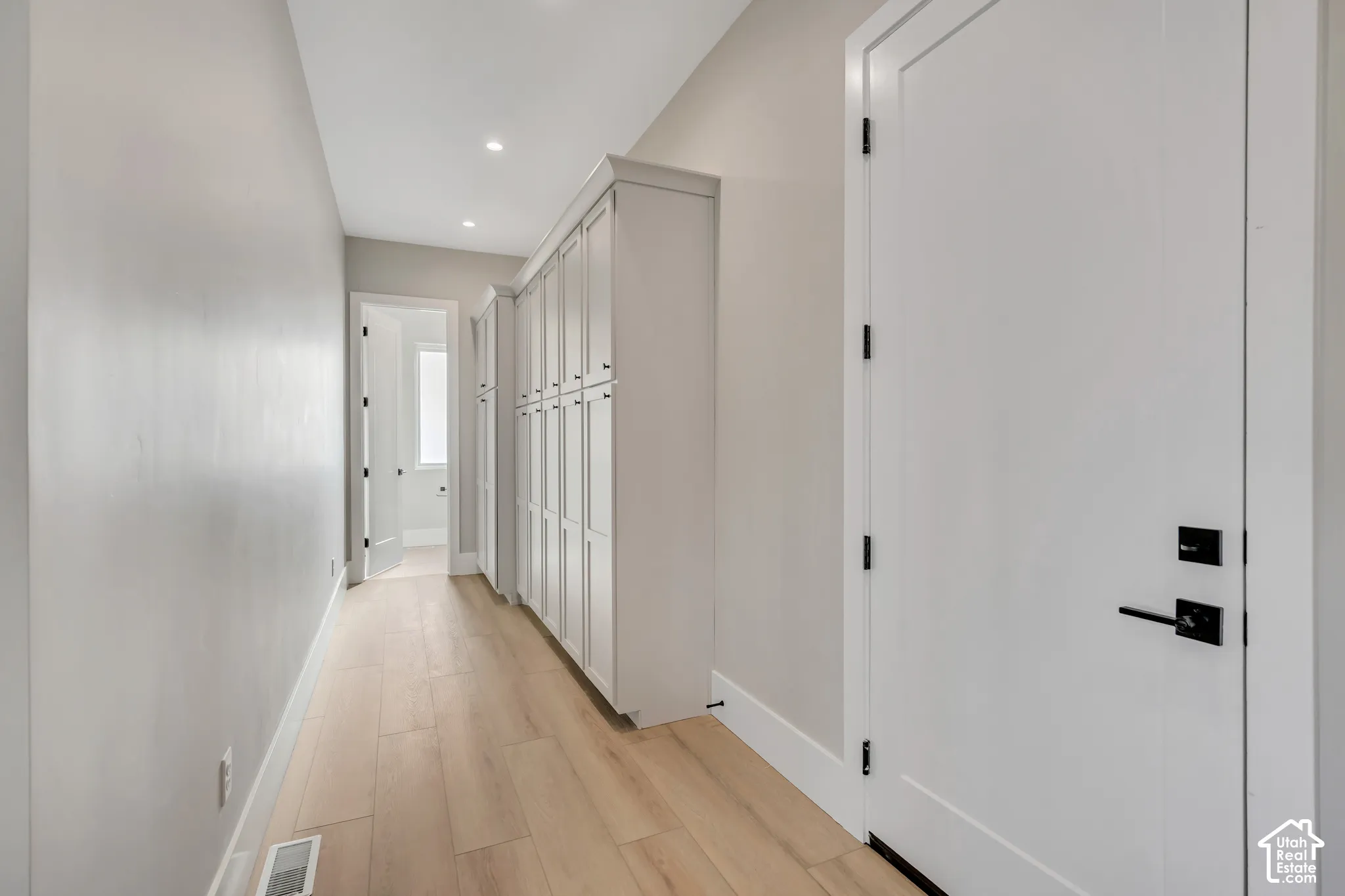 Hallway with wood-finish flooring, built-in white cabinetry, recessed lighting, and white doors with matte black hardware