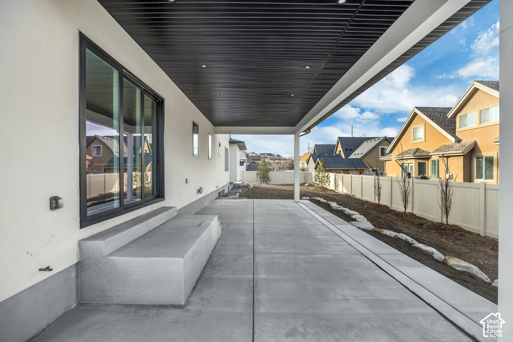 Expansive covered patio with a black slatted ceiling, recessed lighting, and a concrete slab