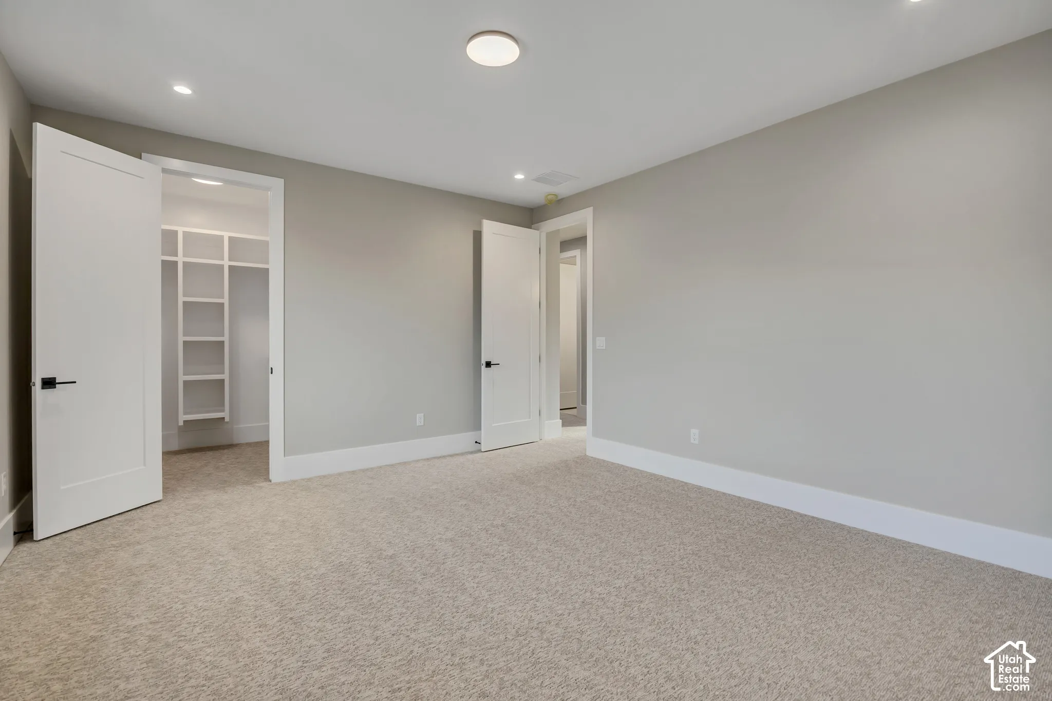 Spacious primary suite featuring neutral wall finishes, recessed ceiling lighting, and direct access to a walk-in closet with built-in shelving