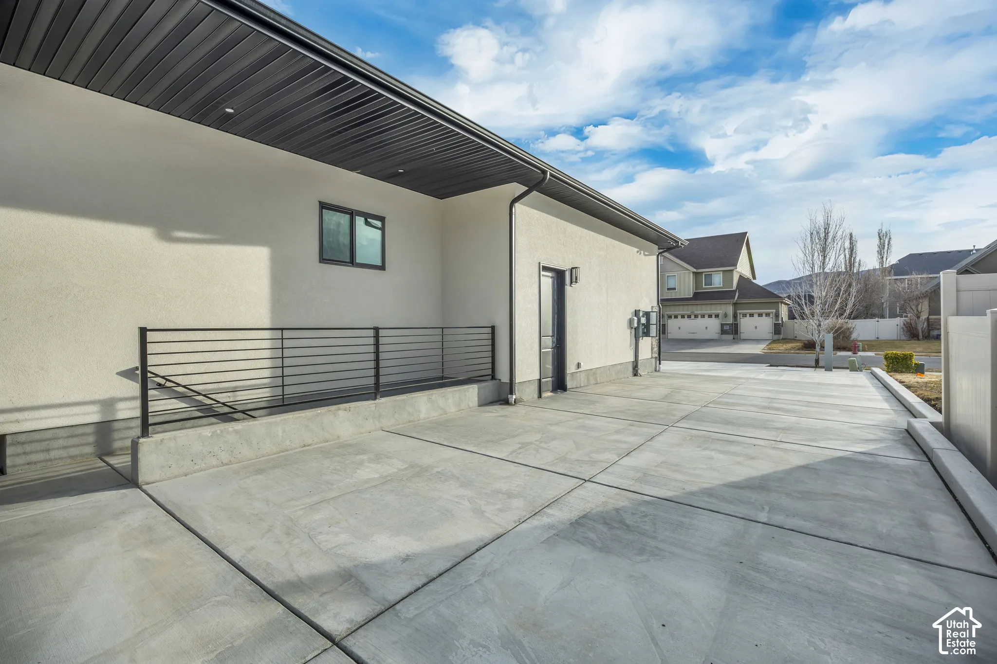 Expansive concrete driveway, stucco exterior, black horizontal railing, dark soffit, and exterior door