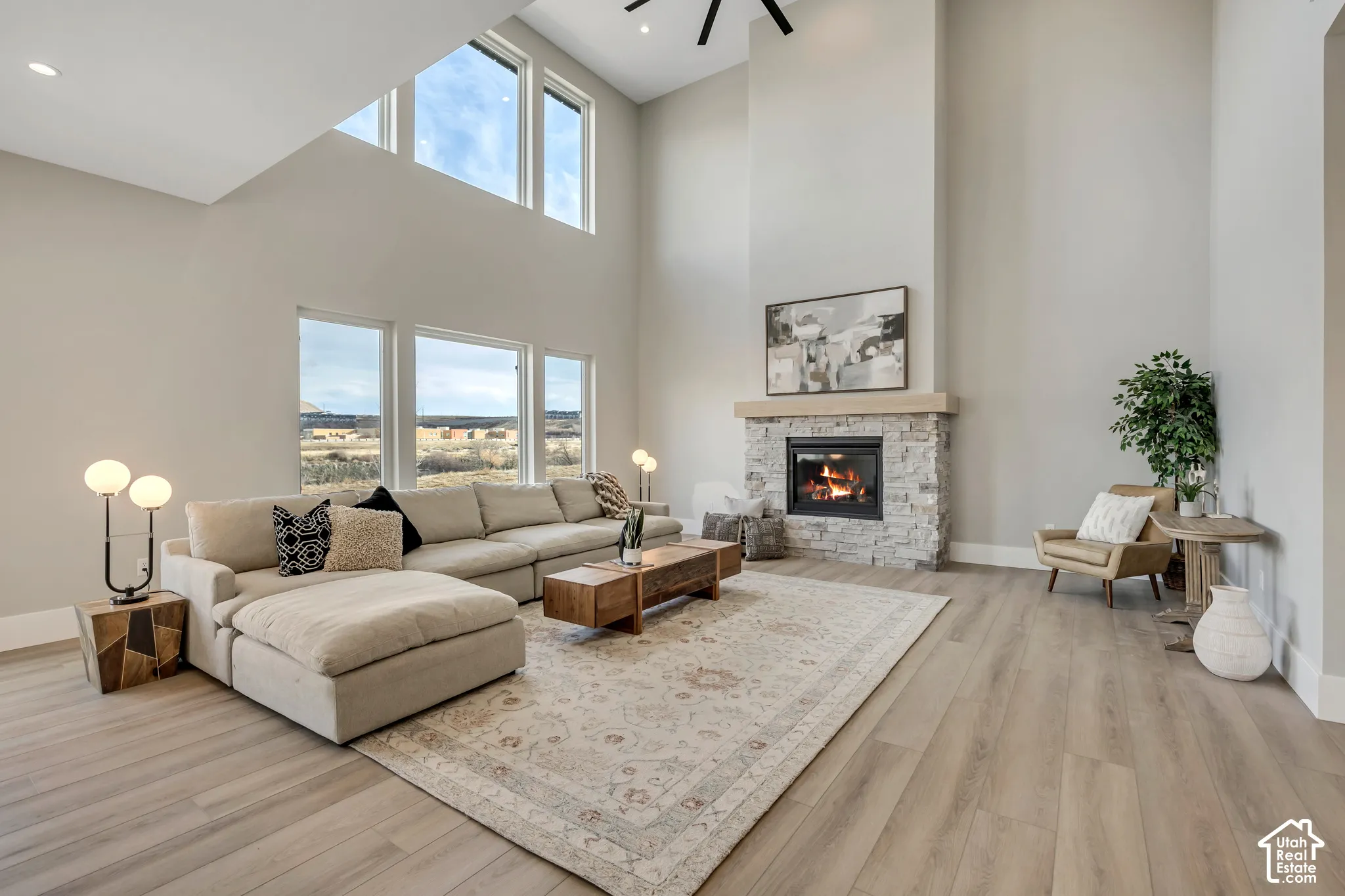 Two-story living area featuring wood-finish flooring, a stone fireplace with a substantial hearth, and multiple large windows