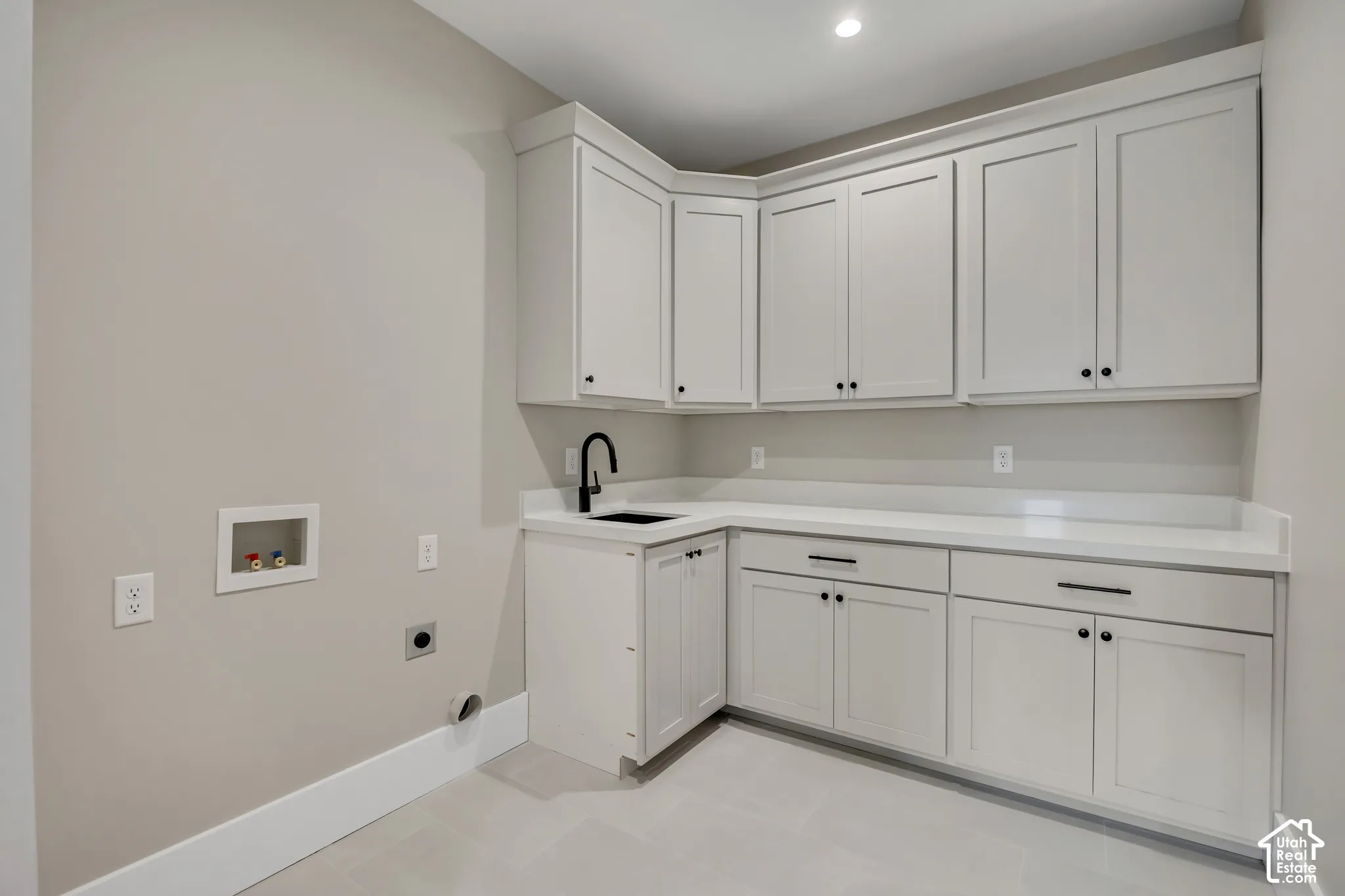 White shaker-style cabinetry with black hardware, light-toned countertops, an undermount sink with a black gooseneck faucet, and recessed lighting