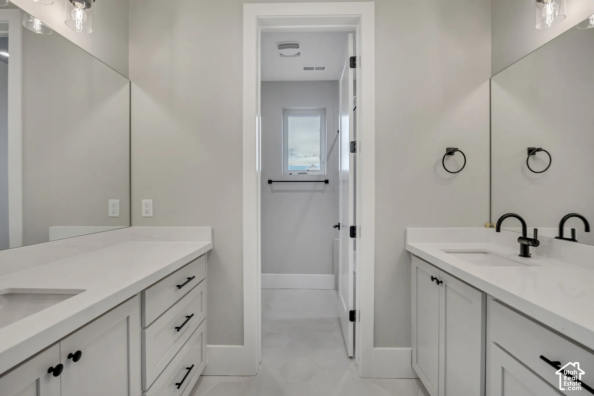 Dual vanity with white cabinetry, white countertops, built-in sinks, matte black hardware, and hexagonal tile flooring