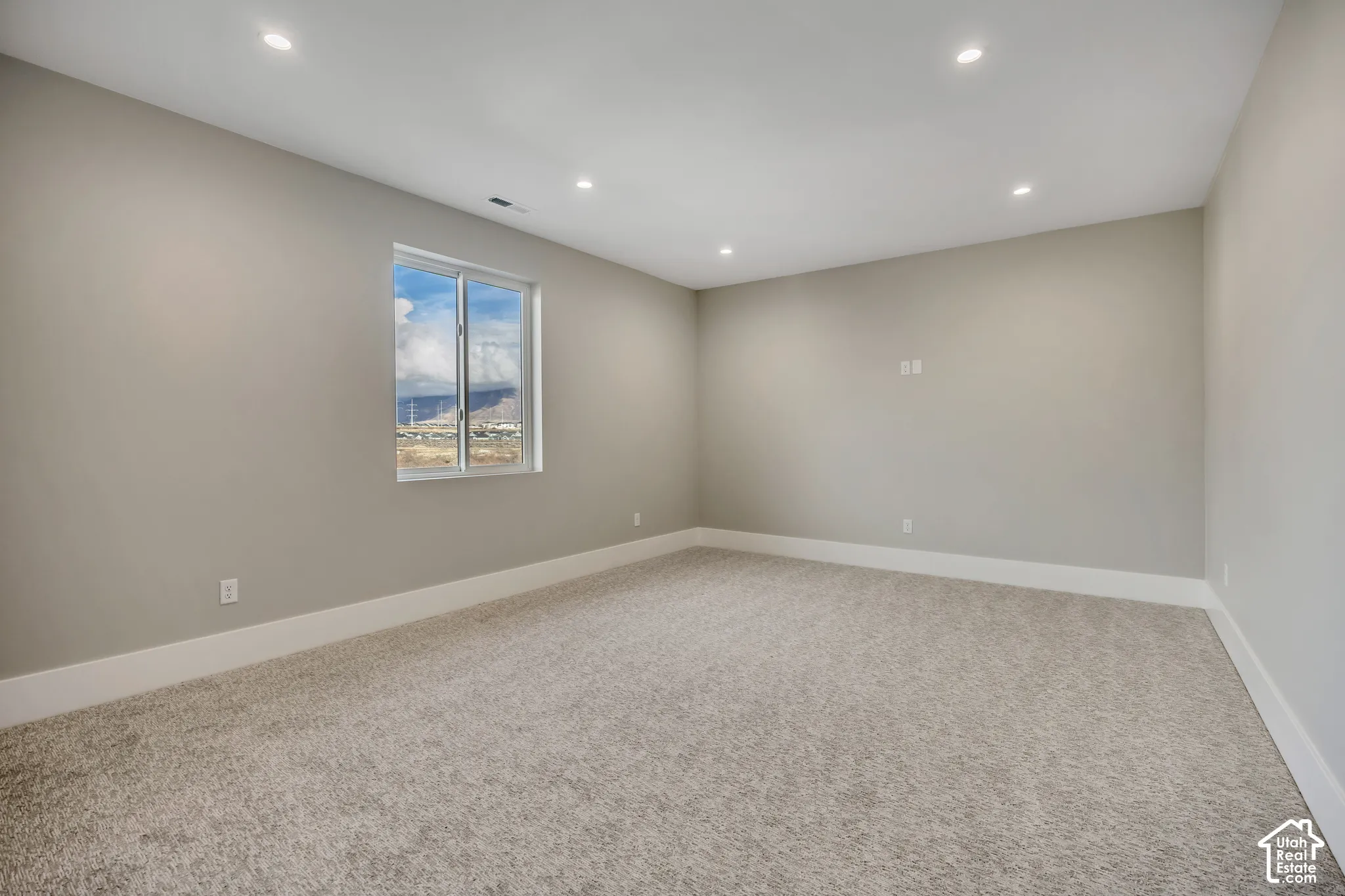 Recessed lighting illuminates this room featuring light gray walls, white trim, and neutral-toned carpeting