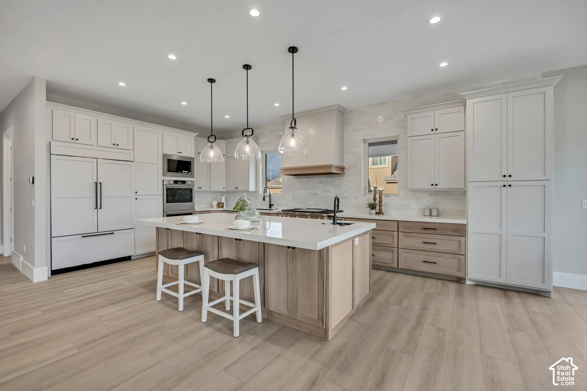 Kitchen featuring wood-finish flooring, white cabinetry, a central island with a light-toned countertop, stainless steel appliances, and pendant lighting