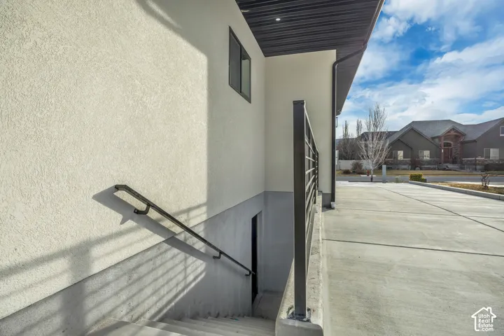Stucco exterior with a compact window, concrete steps with a black metal handrail, and a concrete driveway
