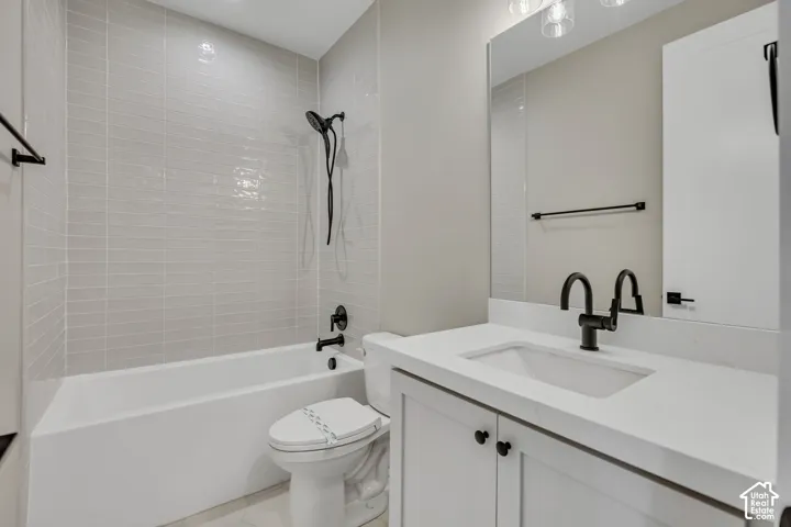 Bathtub with light gray subway tile surround, white vanity with integrated sink, matte black fixtures, and a large wall-mounted mirror