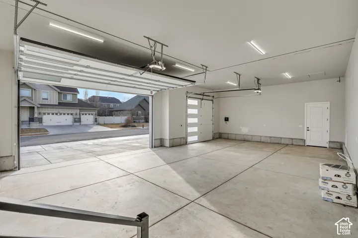 Concrete floor garage with multiple overhead linear light fixtures, an open sectional garage door, and an additional internal door with frosted glass panels