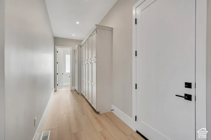 Hallway with wood-finish flooring, built-in white cabinetry, recessed lighting, and white doors with matte black hardware