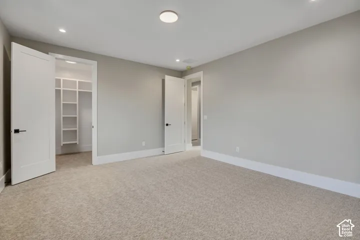 Spacious primary suite featuring neutral wall finishes, recessed ceiling lighting, and direct access to a walk-in closet with built-in shelving