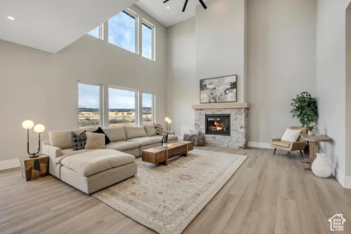 Two-story living area featuring wood-finish flooring, a stone fireplace with a substantial hearth, and multiple large windows