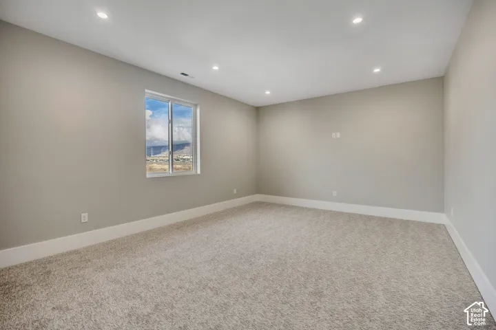 Recessed lighting illuminates this room featuring light gray walls, white trim, and neutral-toned carpeting