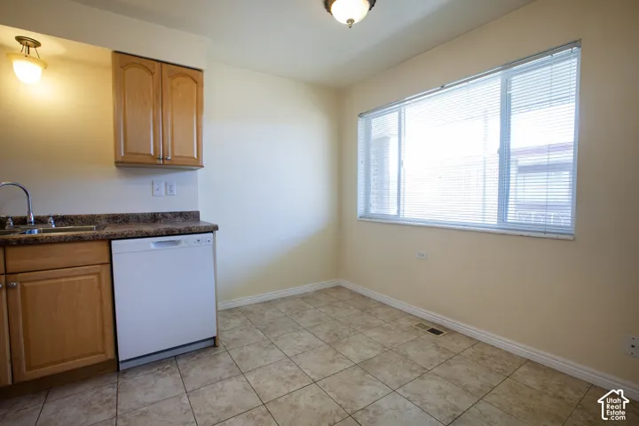 Kitchenette with wood-finish cabinetry, a built-in dishwasher, and a stainless steel sink with a chrome faucet